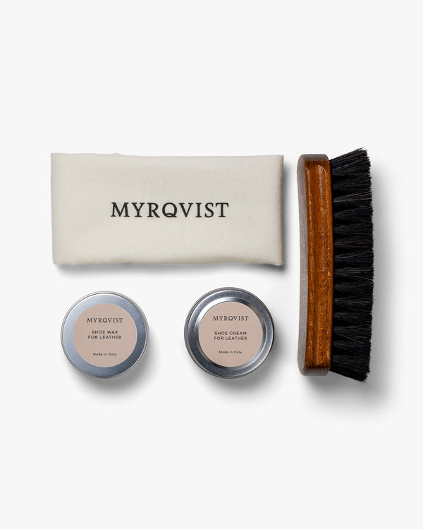 Shoe Care Kit – Leather arranged on a white background, featuring a soft Myrqvist-branded polishing cloth, a wooden-handled brush with dark bristles, and minimalist tins of shoe cream and wax for leather shoe maintenance.