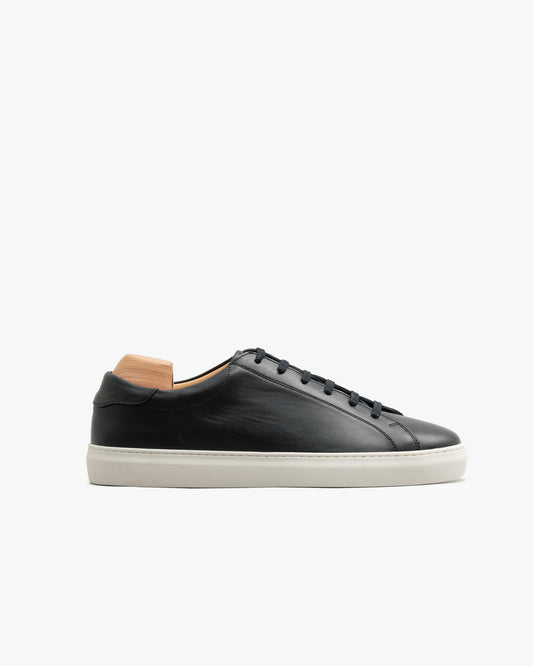 Low-top Oaxen sneaker in black calf leather with a smooth finish, featuring a clean side profile, tonal laces, and a white M-pattern sole, shown with a wooden shoe tree inserted.