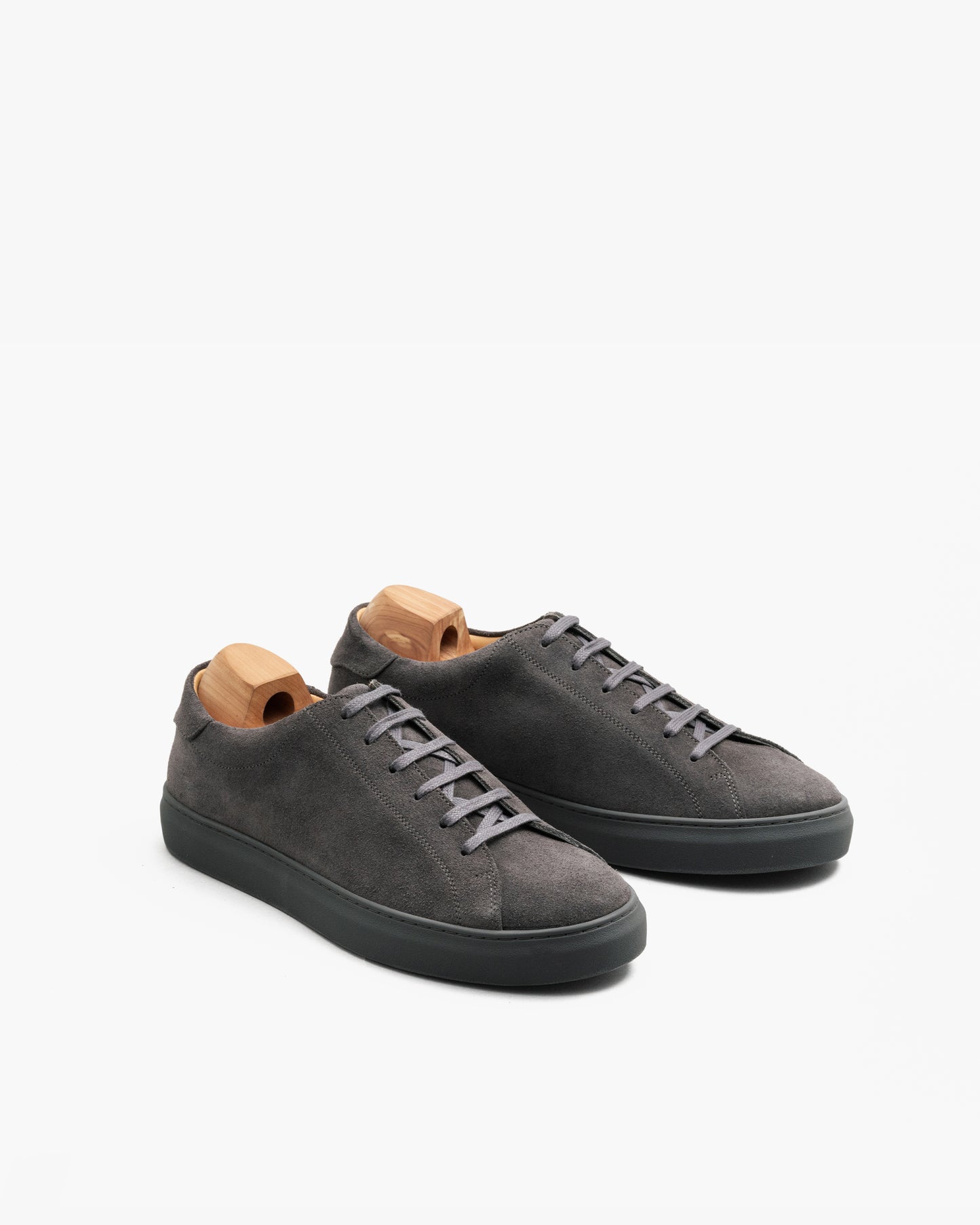 Oaxen Monochrome sneakers in dark grey suede with matching soles and tonal laces, displayed at an angle to highlight the soft suede texture and minimalist design, each shoe fitted with a wooden shoe tree.