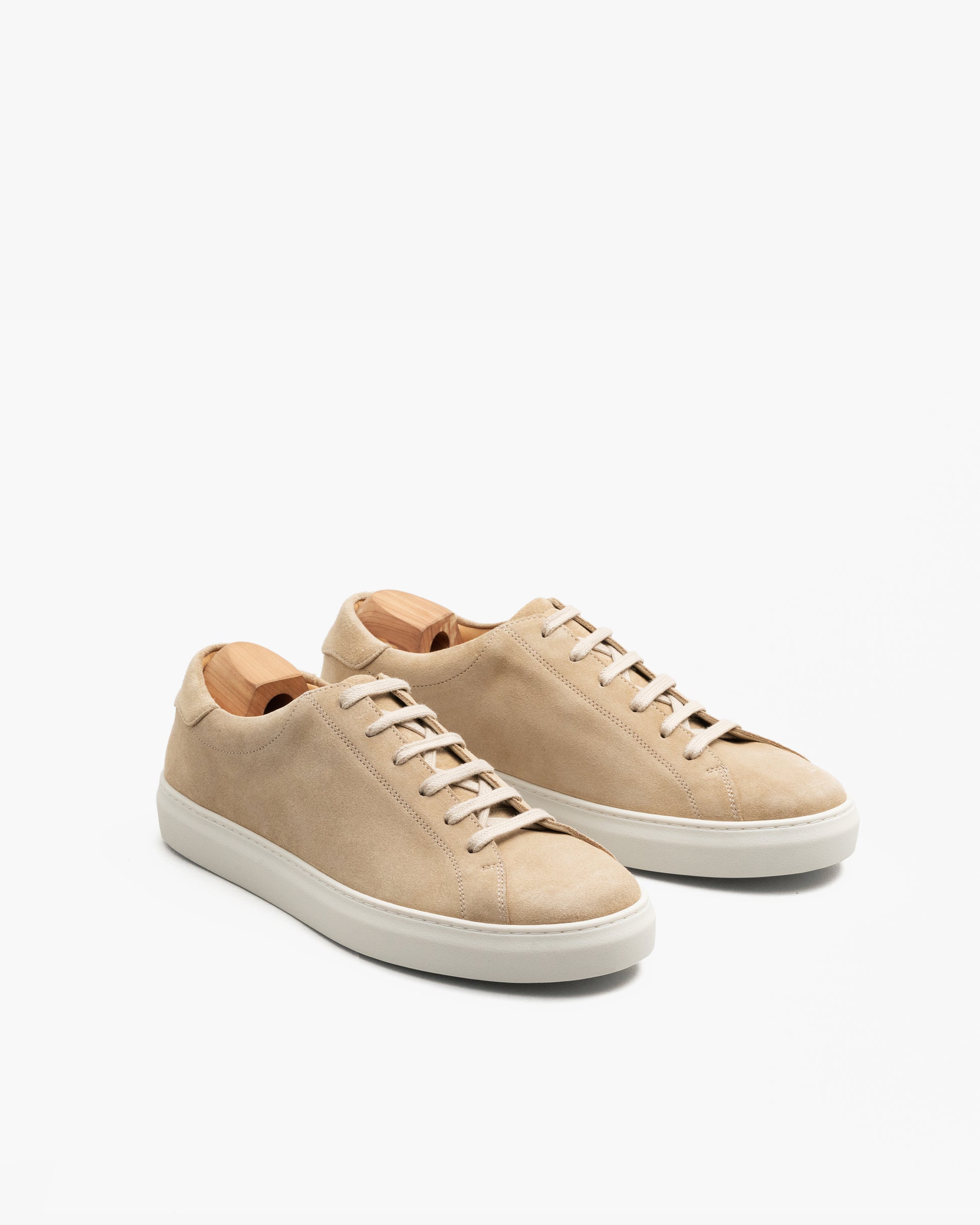 Pair of Oaxen in sand suede shown at an angle, highlighting the soft beige suede upper, tonal laces, minimalist stitching, and off-white sculpted cup soles, with wooden shoe trees inside for shape.