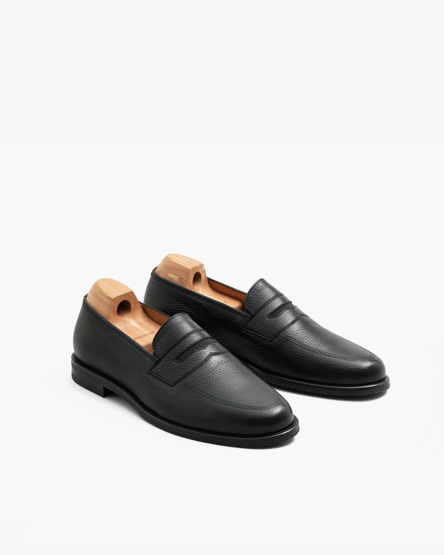 Pair of Sigtuna – Black Natural Grain penny loafers with cedar shoe trees on a plain white background.