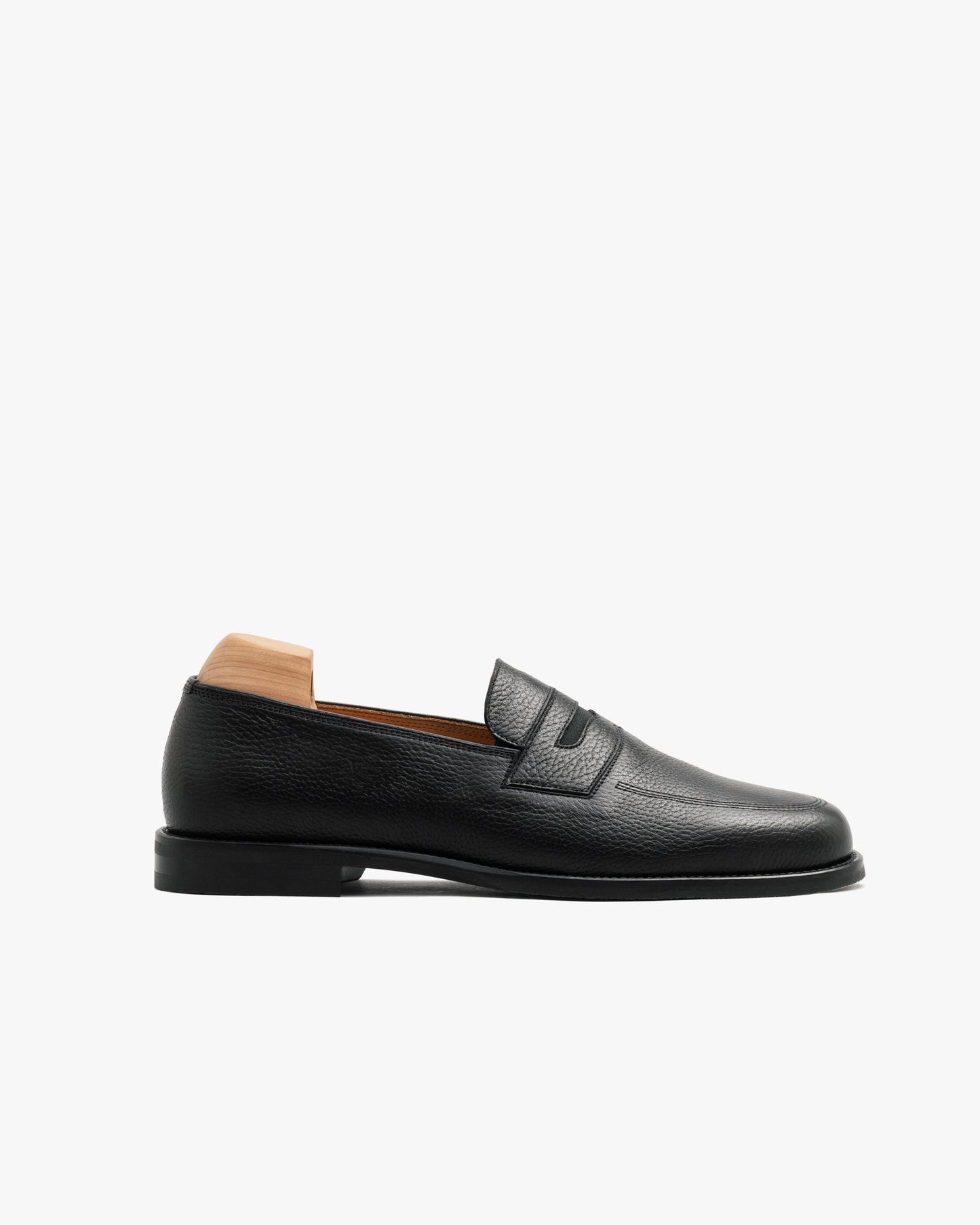 Side profile of Sigtuna – Black Natural Grain penny loafer in textured leather with a wooden shoe tree inside.