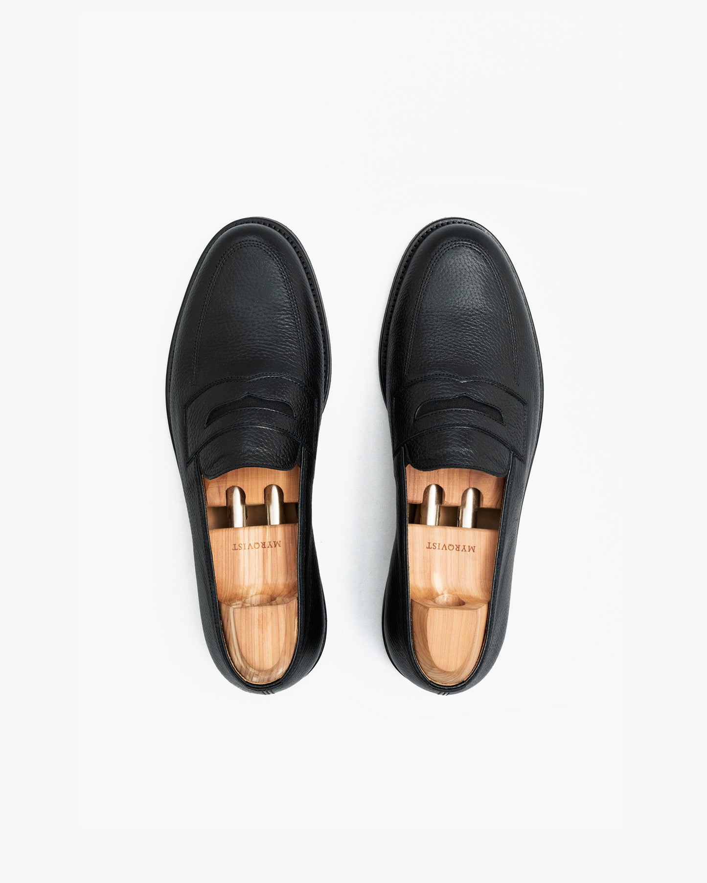 Top-down view of Sigtuna – Black Natural Grain loafers with wooden shoe trees on a white background.