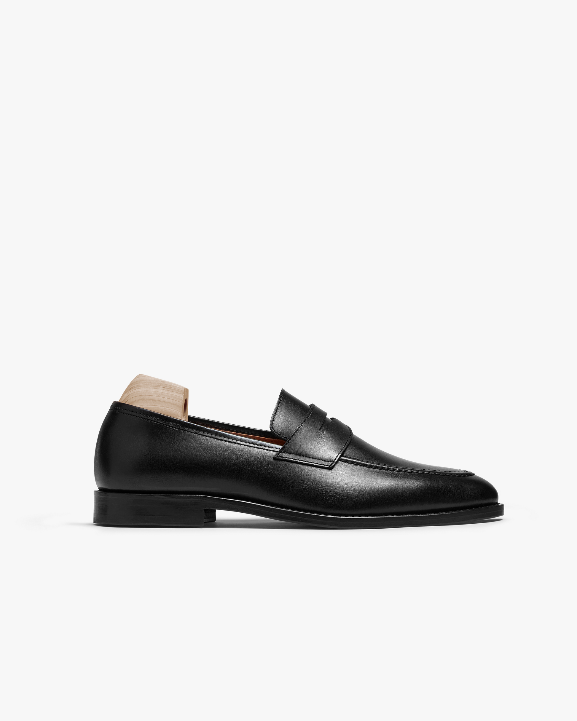 Smögen loafer in black calf, shown in profile, features smooth full-grain leather with a gently rounded toe, clean stitching, and a classic penny strap, set on a low black sole with a wooden shoe tree in the heel.