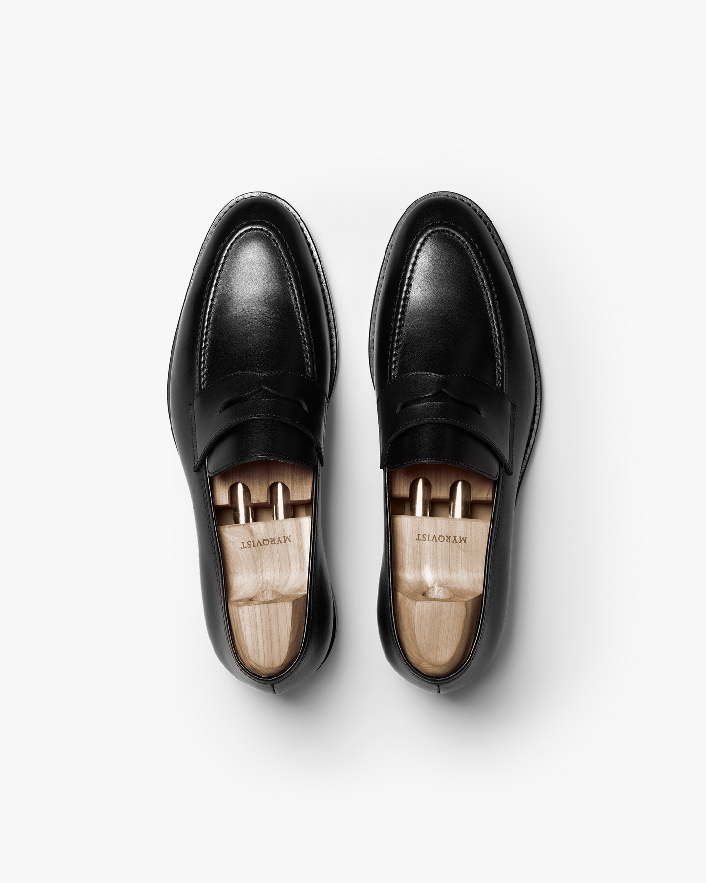 Pair of Smögen loafers in black calf leather, viewed from above, highlighting the clean lines, penny strap detail, and wooden shoe trees inside each shoe.