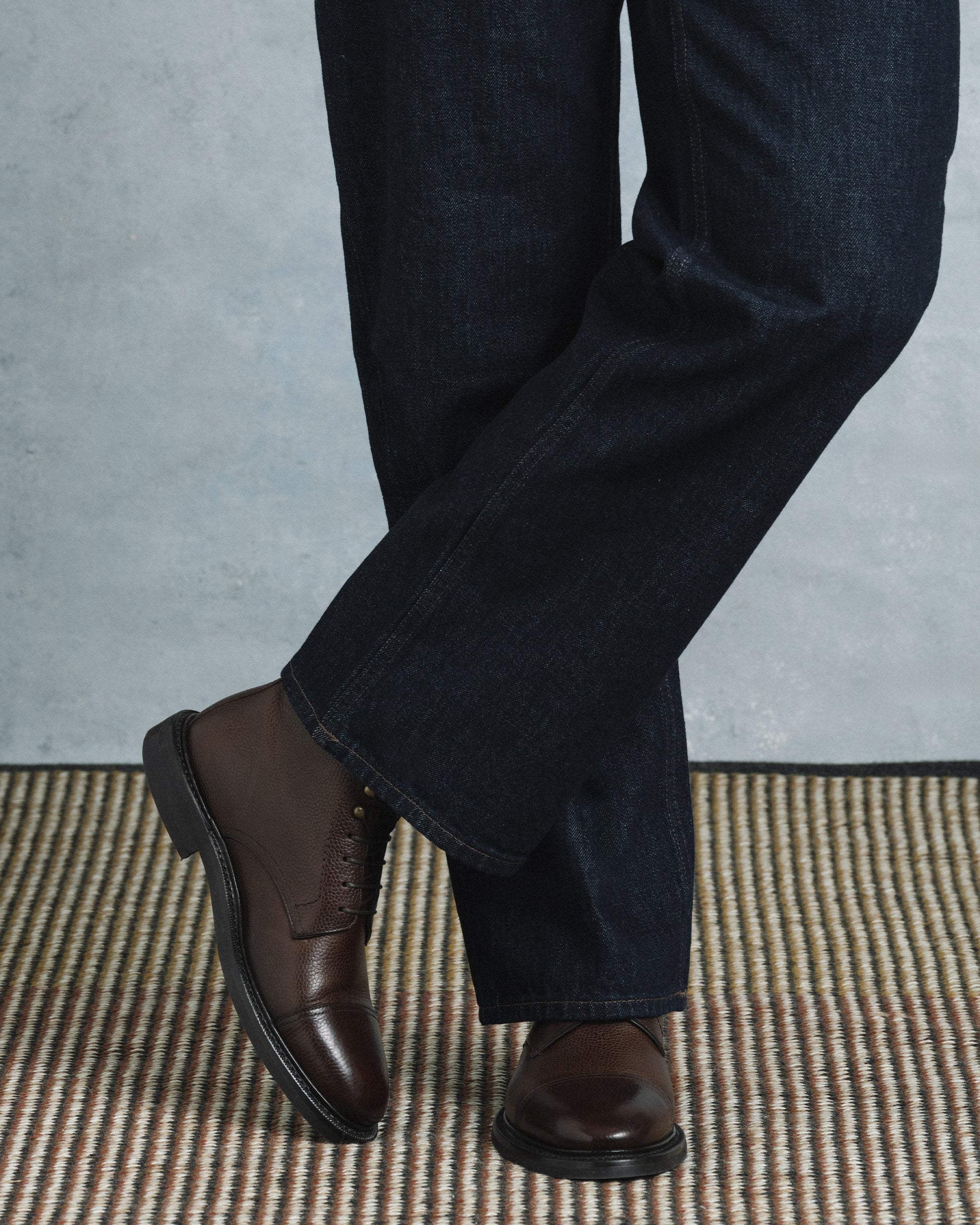 Abisko in dark brown country calf worn with dark denim, showcasing the textured grained leather, cap toe, and sturdy rubber sole for a refined yet versatile style suitable for both casual and dressed-up occasions.