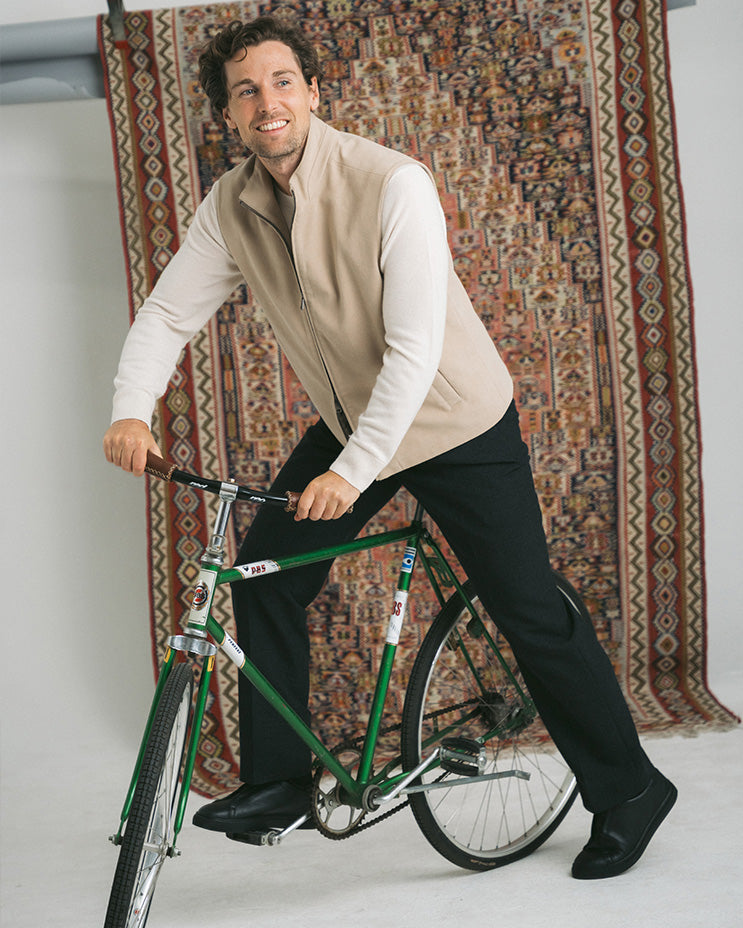 Man on a bicycle wearing Alnö Shearling – Black Natural Grain sneakers with dark slacks and a beige vest.