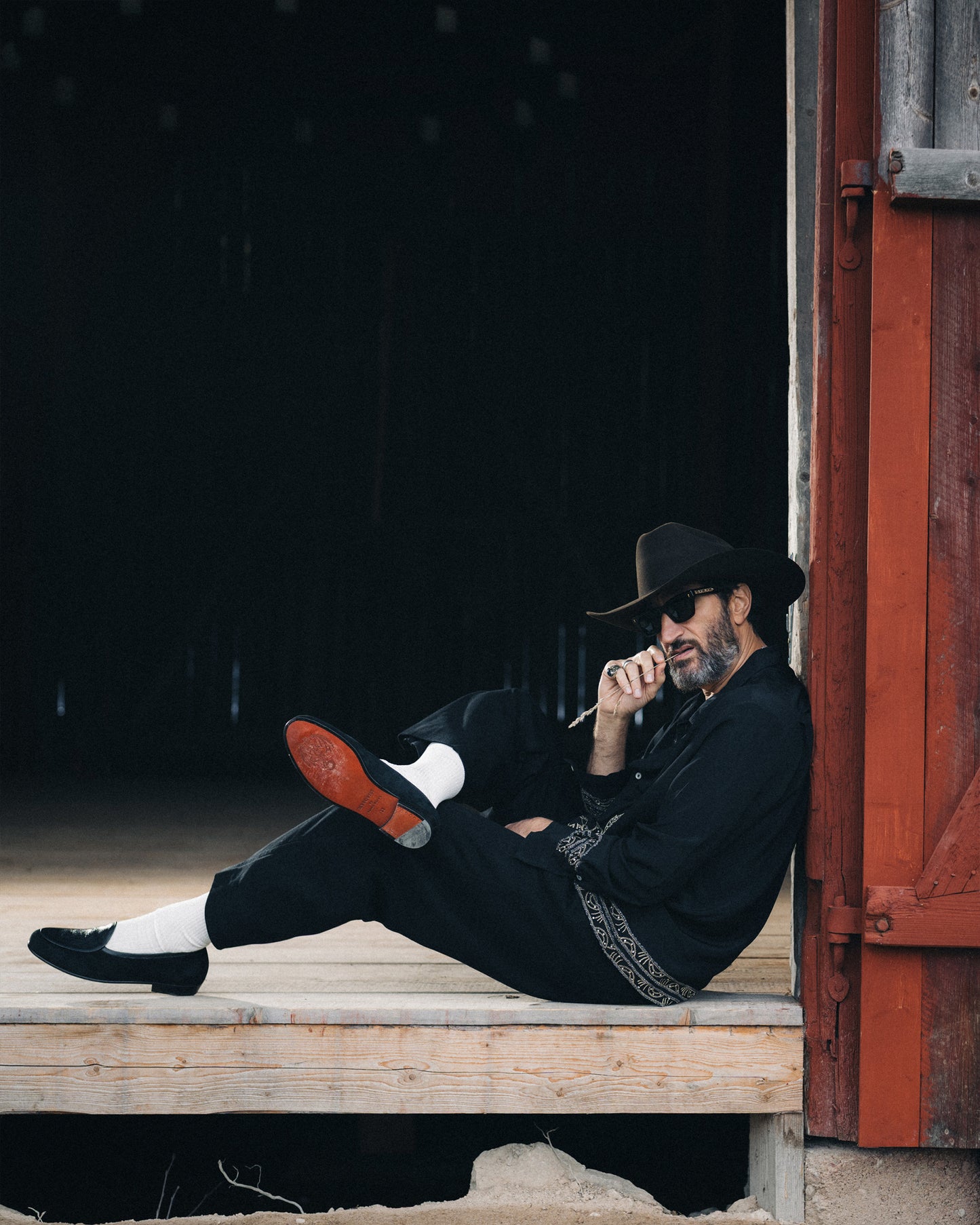 Fares Fares models Ängby – Fares Edition shoes, sitting in a doorway while showcasing the contrasting red sole.
