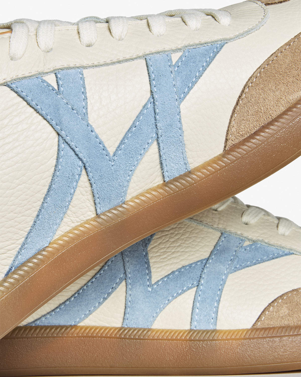 Högalid – White Natural Grain close-up of two stacked shoes showing the pale blue suede M logo and gum midsole.