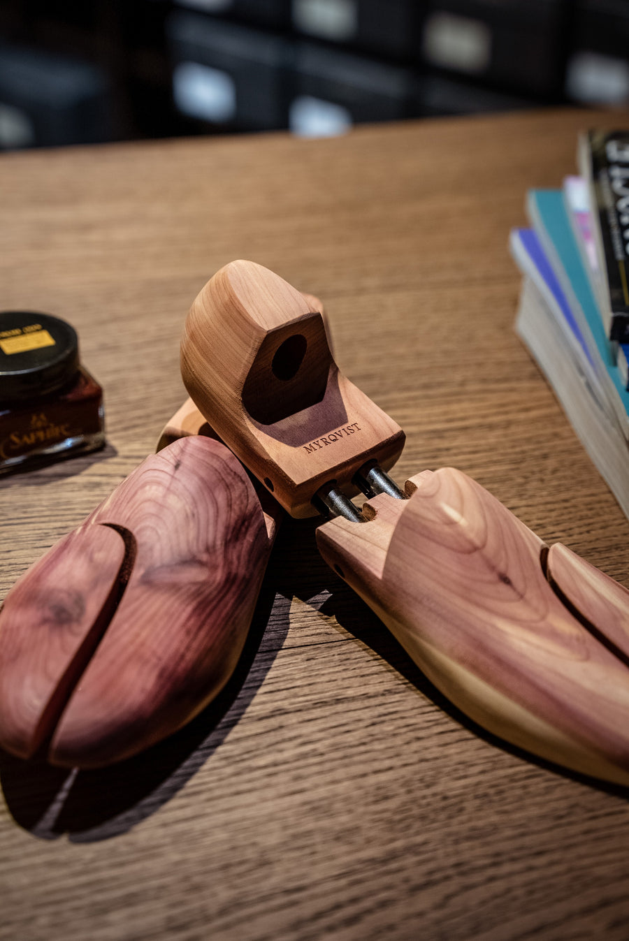 A pair of wooden cedar shoe trees resting on a wooden counter beside a tin of shoe cream.