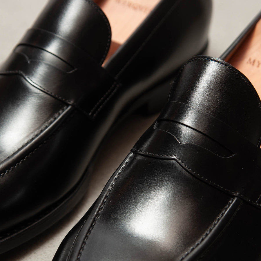 Close-up of two black leather loafers with a high mirror shine on the toes.