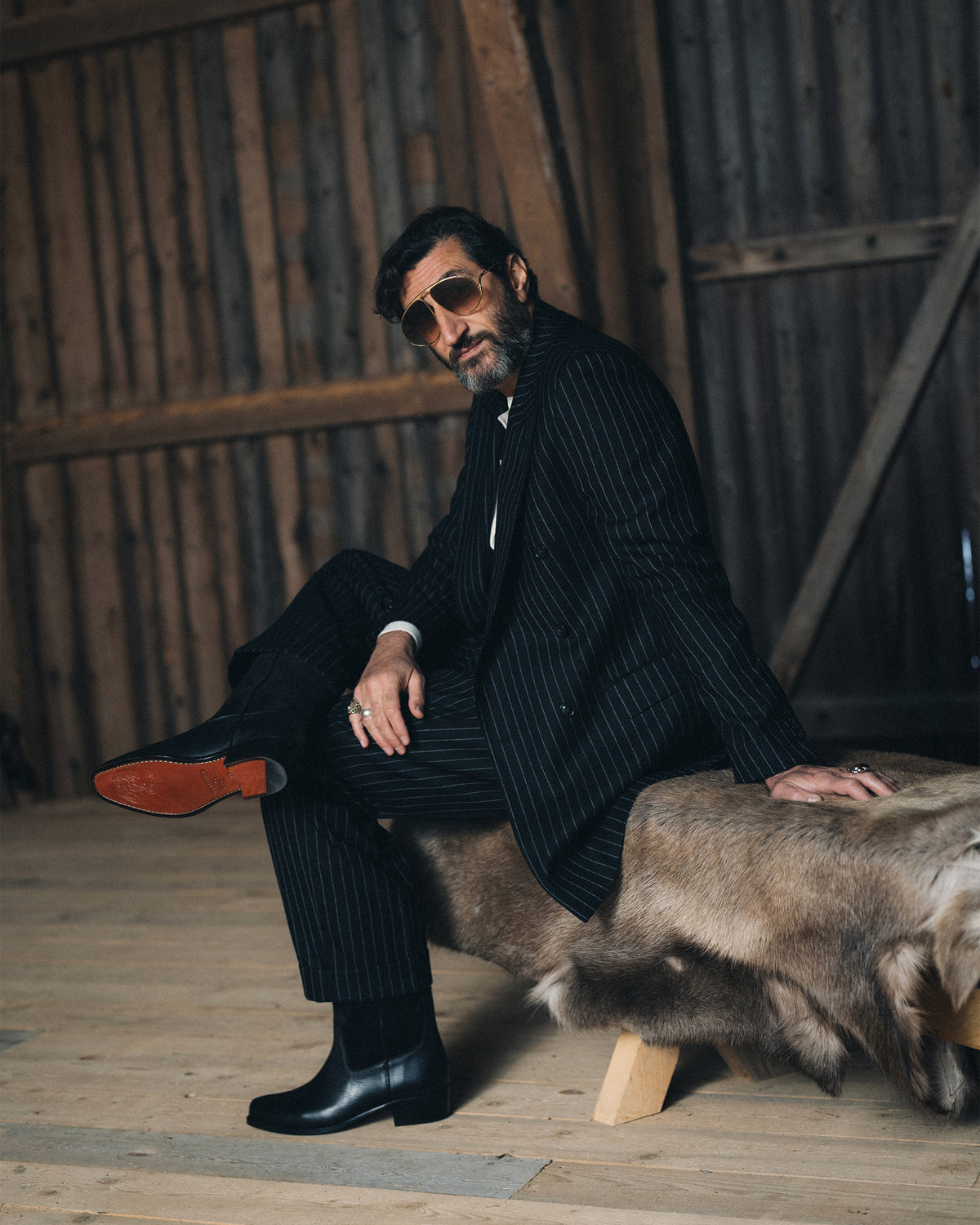 Karlslund – Black boots worn by Fares Fares with a pinstripe suit and sunglasses in a rustic setting.