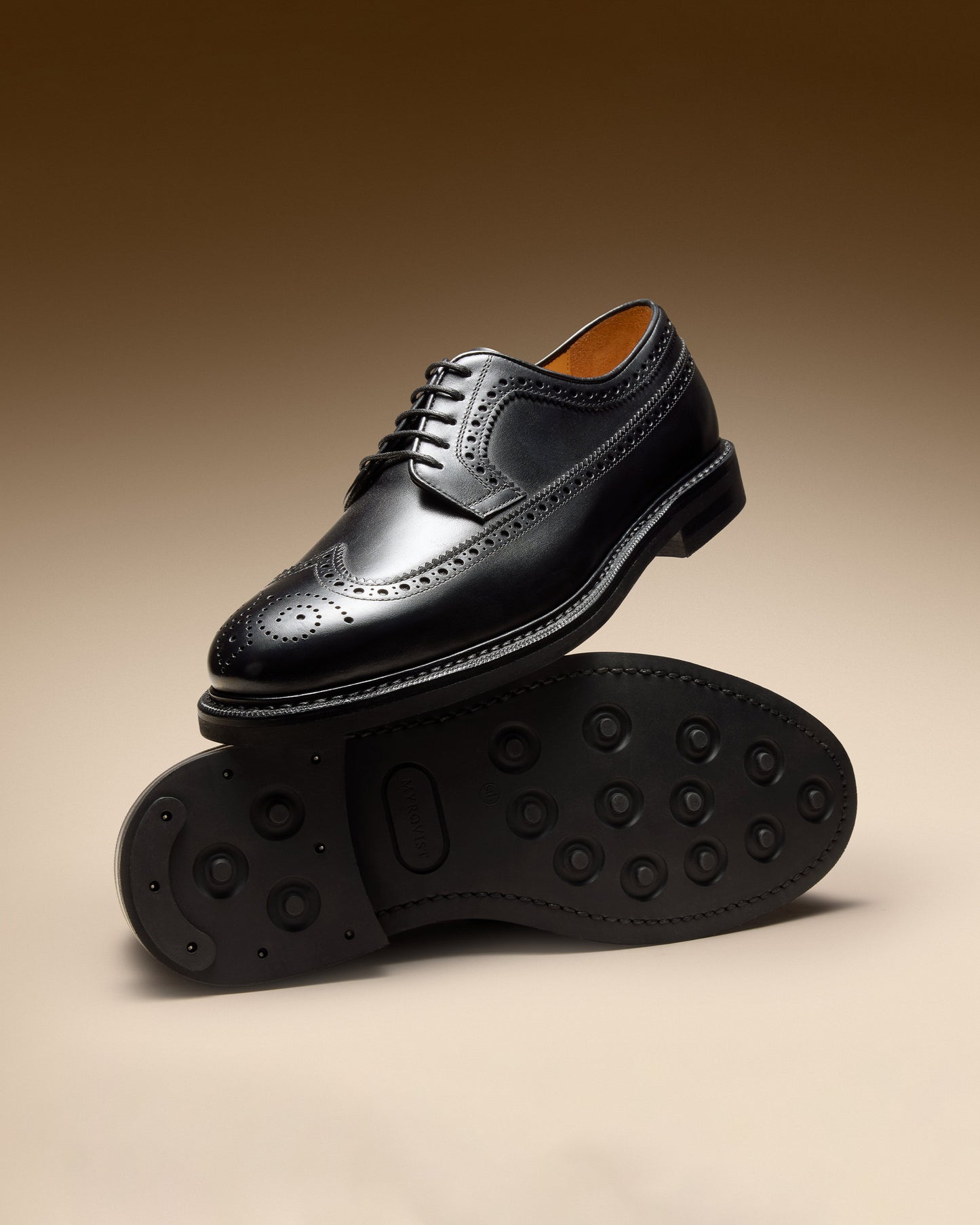 Side profile of Orust II – Black Calf brogue derby resting on its mate's studded rubber sole against a brown background.