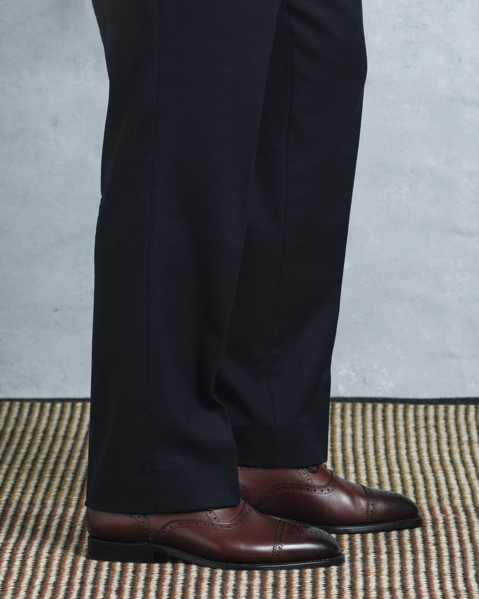 Strömsö II in dark mahogany calf, a semi-brogue Oxford with cap toe and subtle perforations, styled with tailored navy slacks for a refined, formal look.