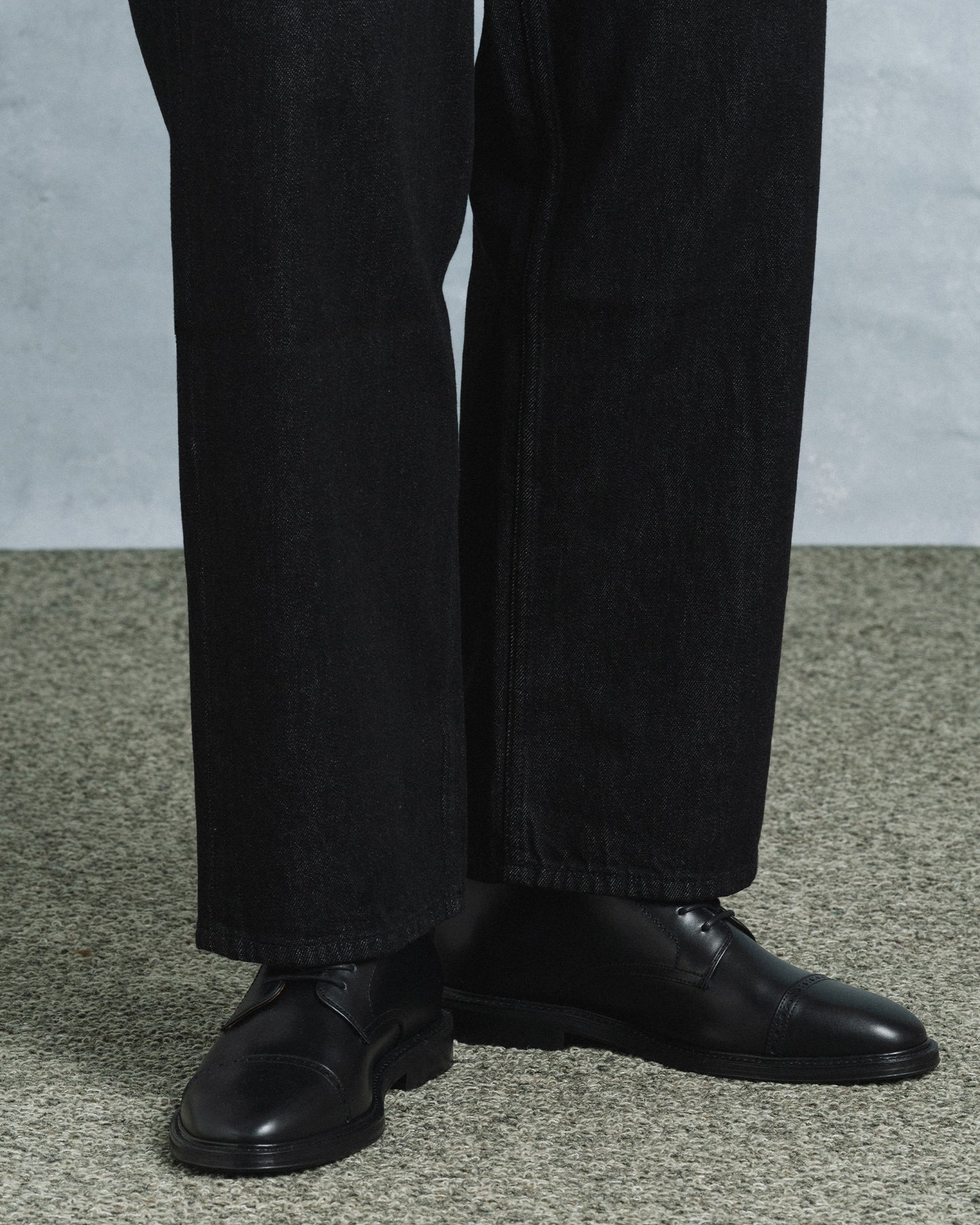 Tjärnö II in black calf styled with dark denim, showcasing the polished cap toe, subtle broguing, and versatile silhouette ideal for both casual and formal outfits.