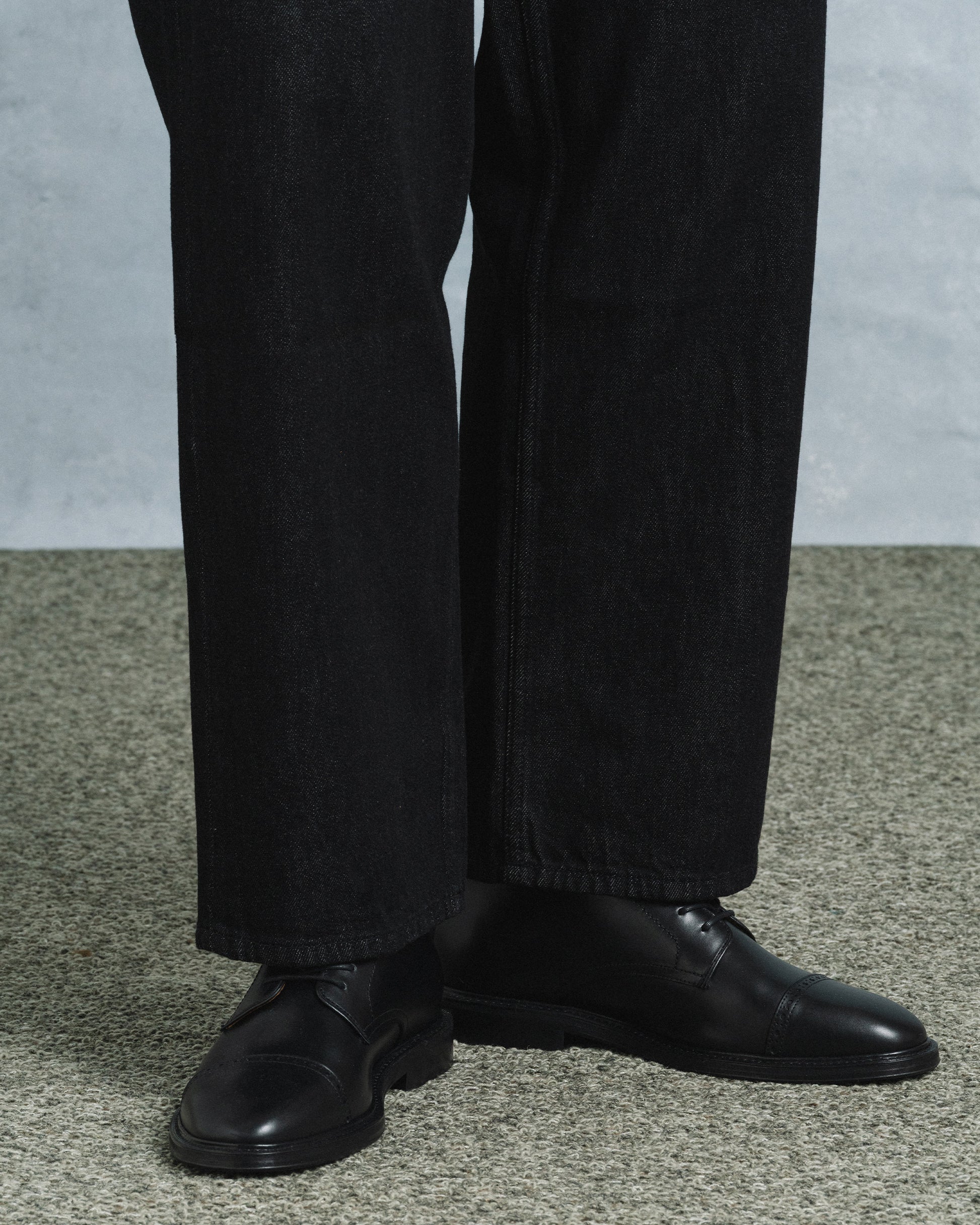 Tjärnö II in black calf styled with dark denim, showcasing the polished cap toe, subtle broguing, and versatile silhouette ideal for both casual and formal outfits.