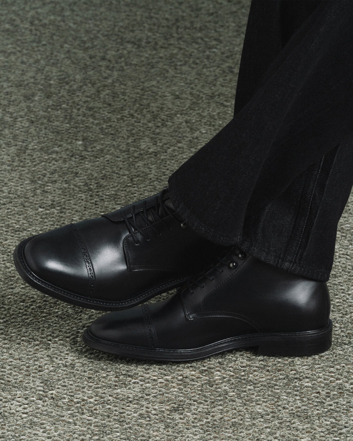 Tjärnö II in black calf worn with dark denim, highlighting the sleek cap toe, subtle broguing, and versatile design suited for both formal and casual settings.