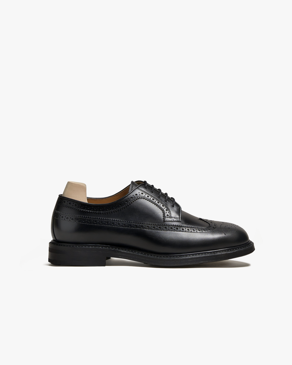 Orust II in black calf features a classic full brogue derby design with intricate wingtip perforations, open lacing, and a sturdy black studded sole, shown in a side profile against a clean white background.