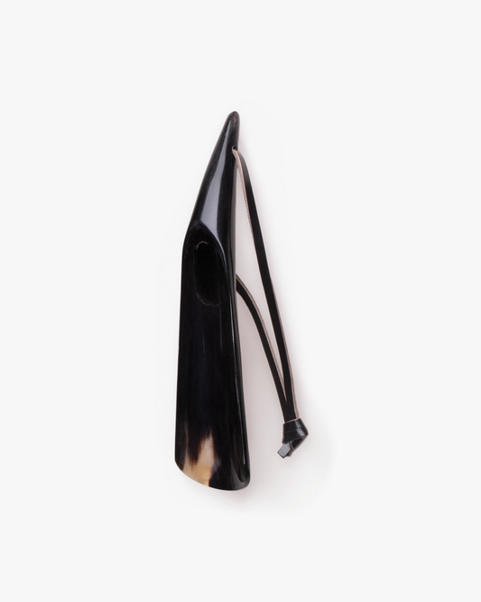 A polished shoe horn crafted from dark cow horn with a leather strap, shown on a white background.